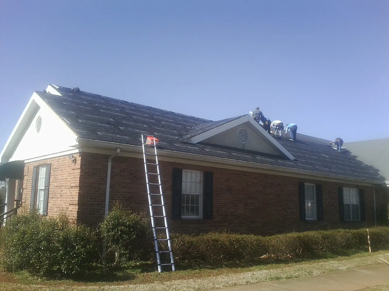 Crew tearing shingles off a brick ranch roof with a ladder set — Metal Roof Repair work by our crew in Culleoka
