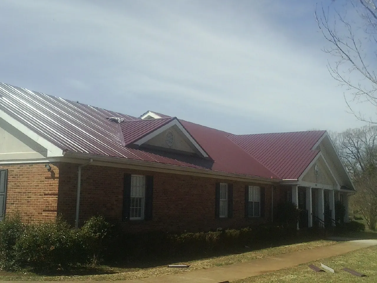 Red metal roof with gabled entries on a long brick building, from a Hail Damage Roof Repair job in Culleoka