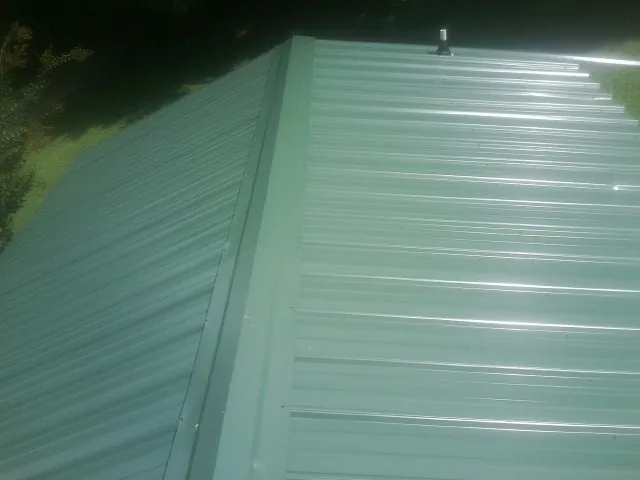 New green metal panels meeting at the ridge of a roof — Flat Roof Repair work by our crew in Culleoka