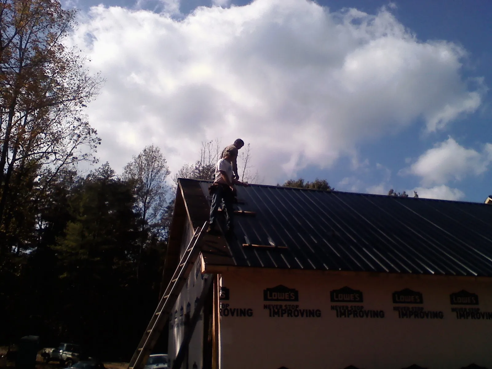 Roofer fastening dark metal panels high against a cloudy sky, from a Roof Inspection job in Culleoka