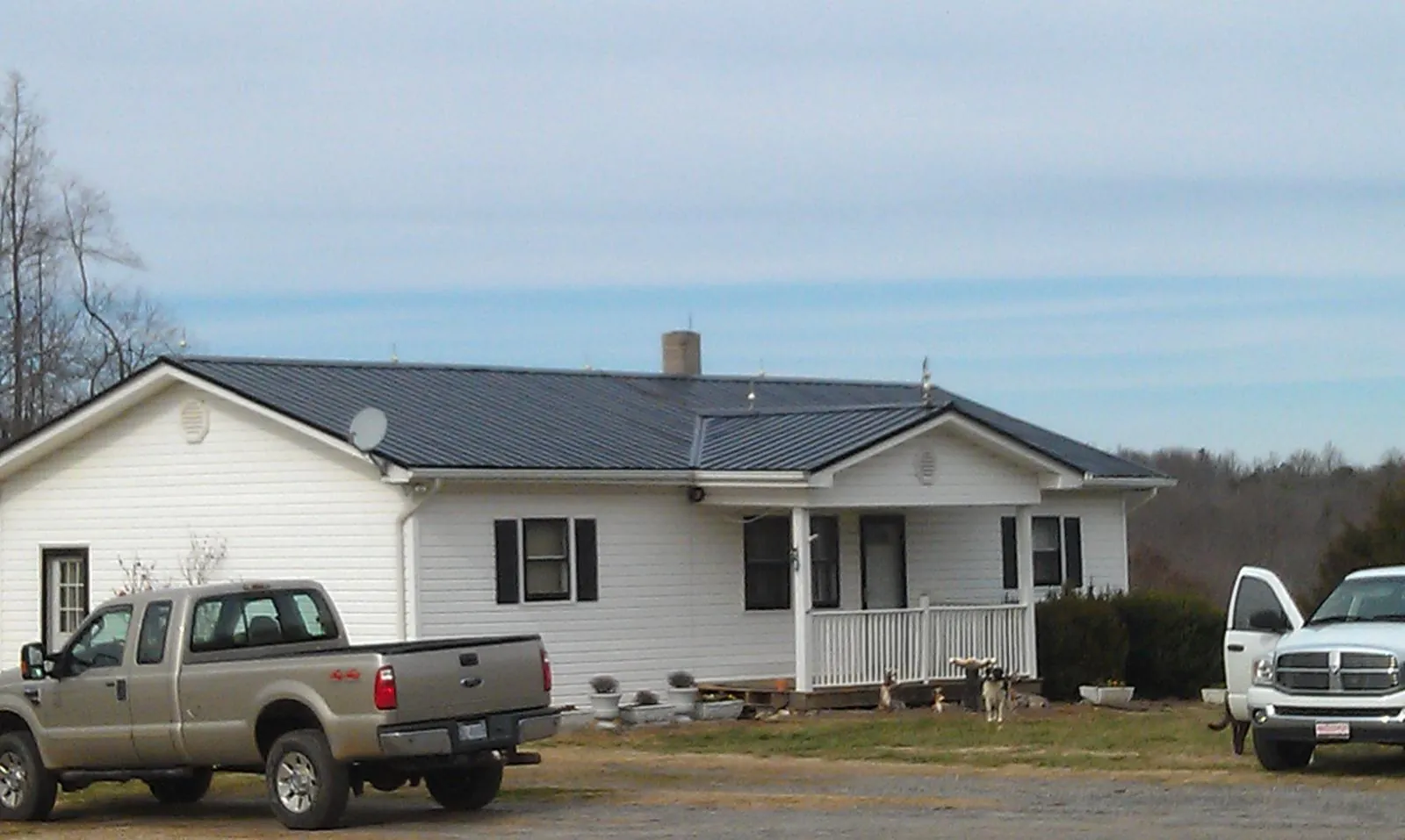 Finished dark metal roof on a white ranch home with work trucks parked in Culleoka