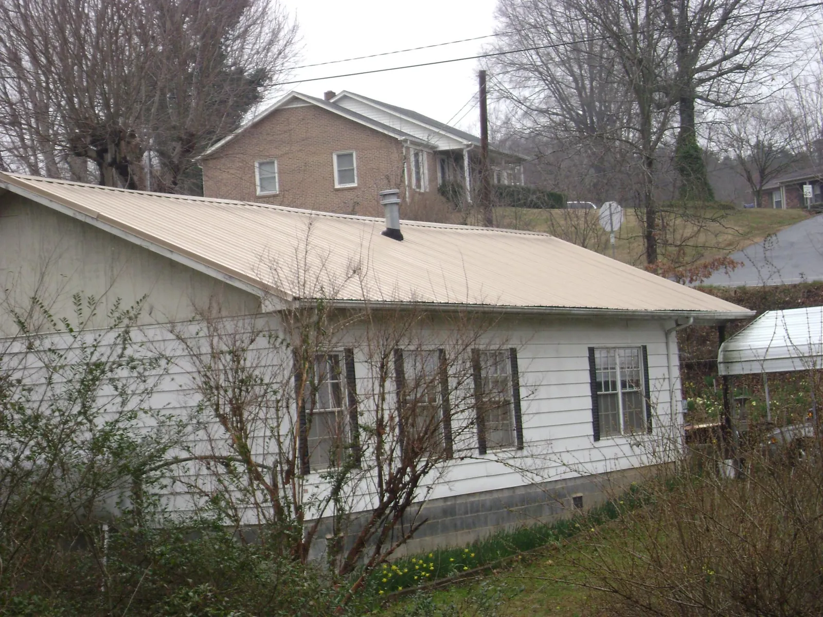 Tan metal roof on a white sided house set into a hillside — Commercial Roofing by Roofing Brothers in Culleoka