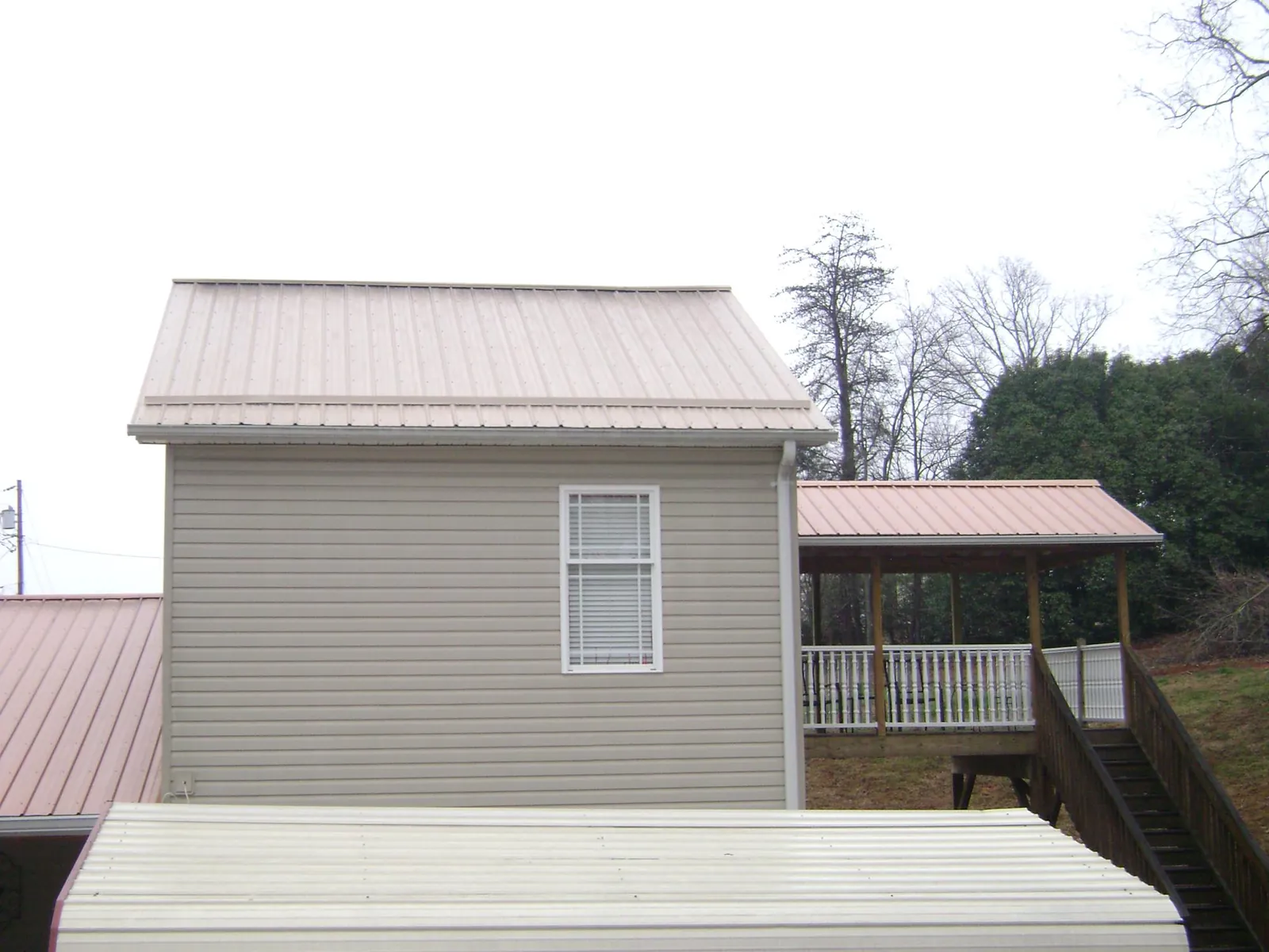 Tan metal roofs on a two story addition and attached porch, from a Roof Replacement job in Culleoka